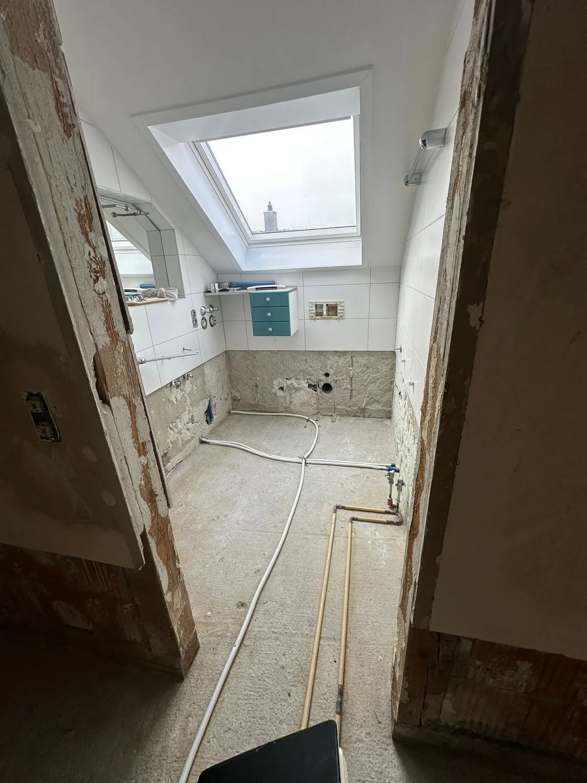 Entkerntes Badezimmer unter dem Dachfenster mit neuen Leitungen