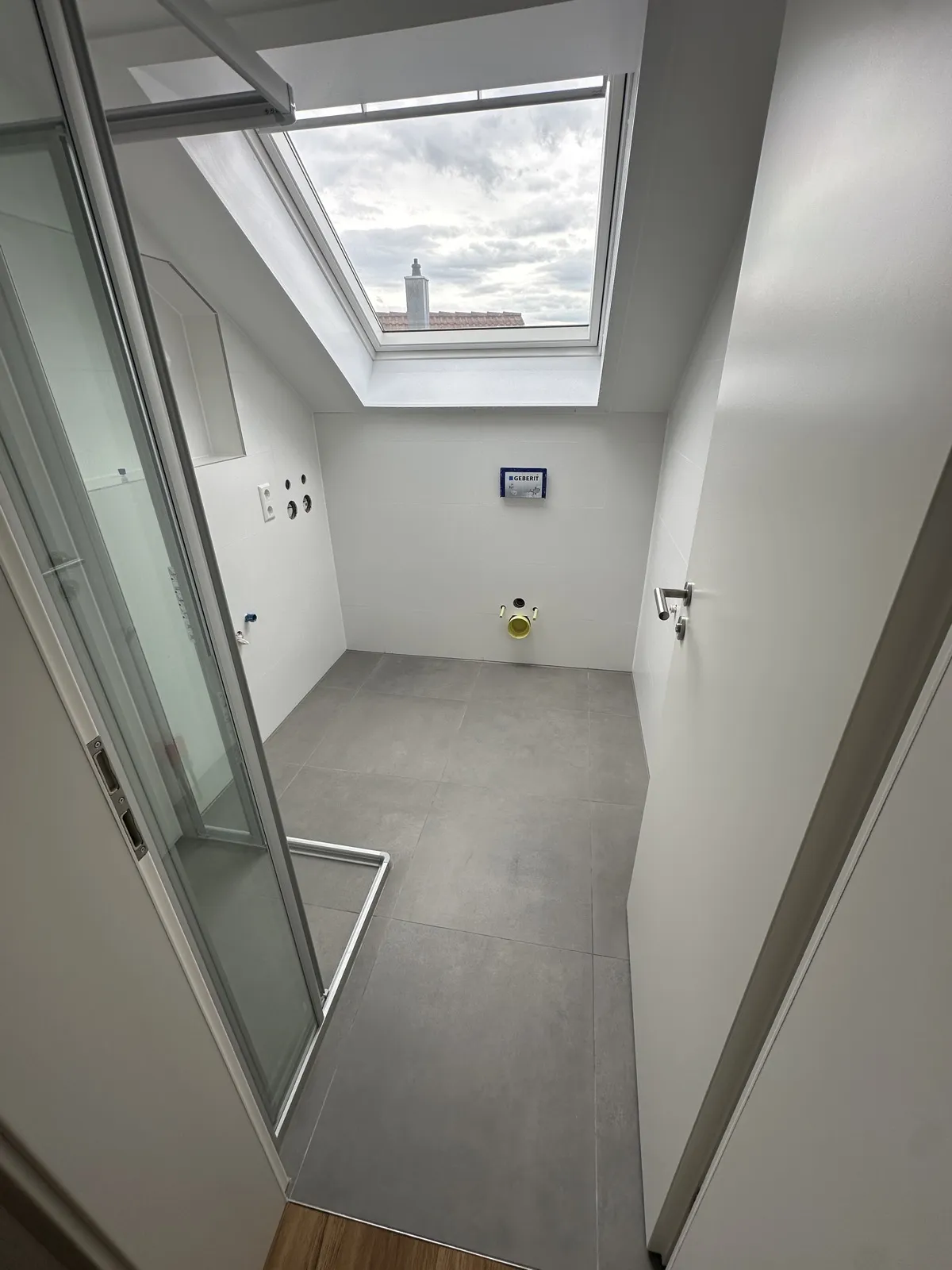 Modernisiertes Badezimmer mit Dachfenster und großformatigen grauen Bodenfliesen
