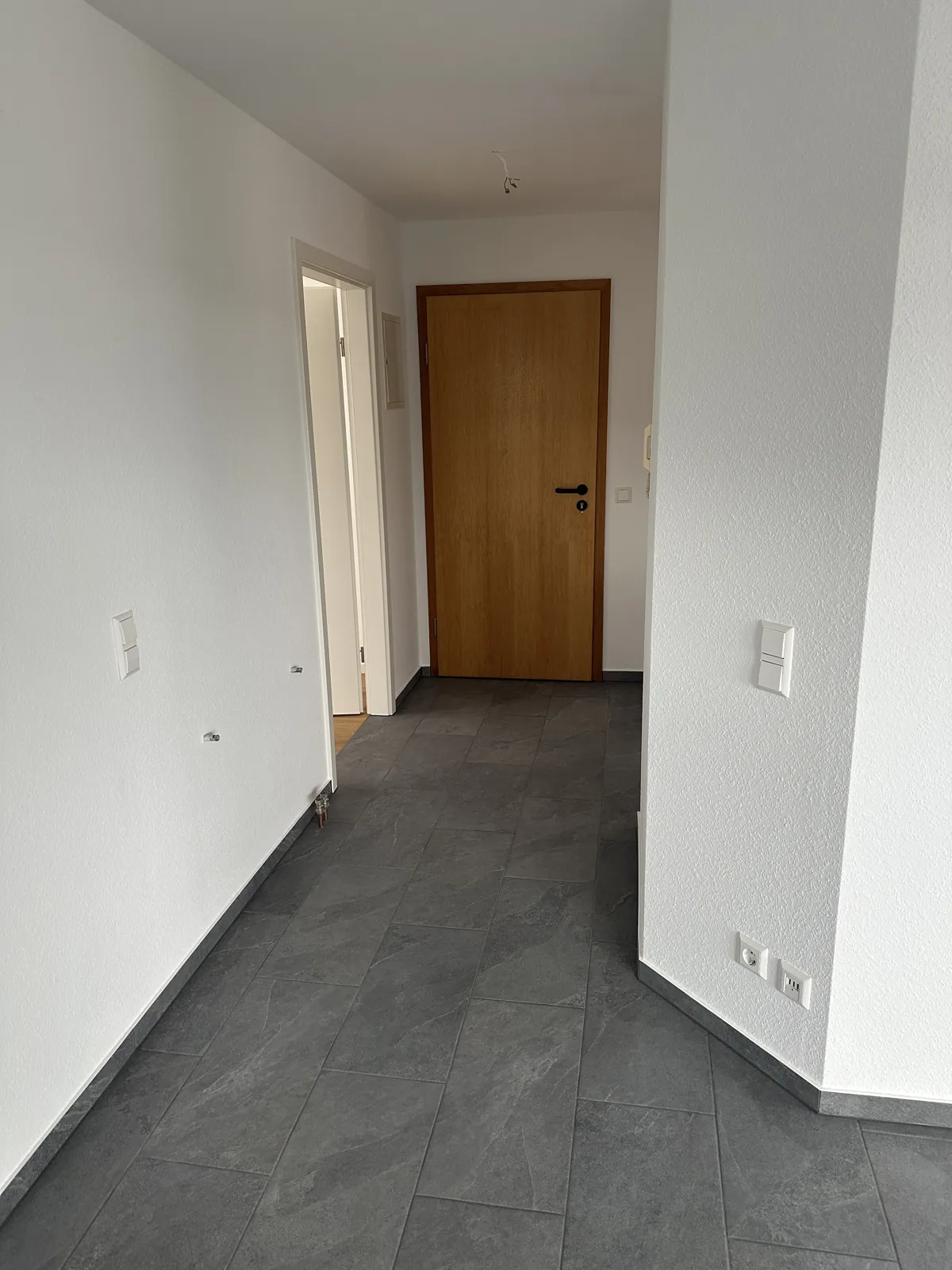 Fertiger Flur mit grauen Feinsteinzeug-Fliesen und weißen Wänden Richtung Wohnungstür