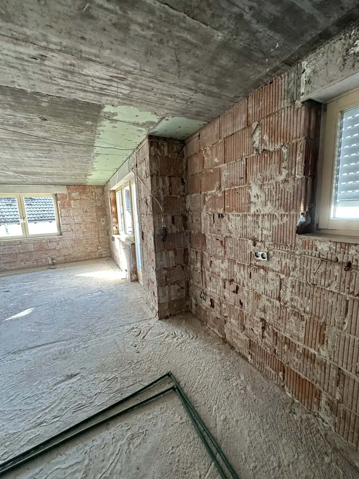 Entkerntes Wohnzimmer mit freigelegten Ziegelwänden und Rohboden nach dem Wasserschaden