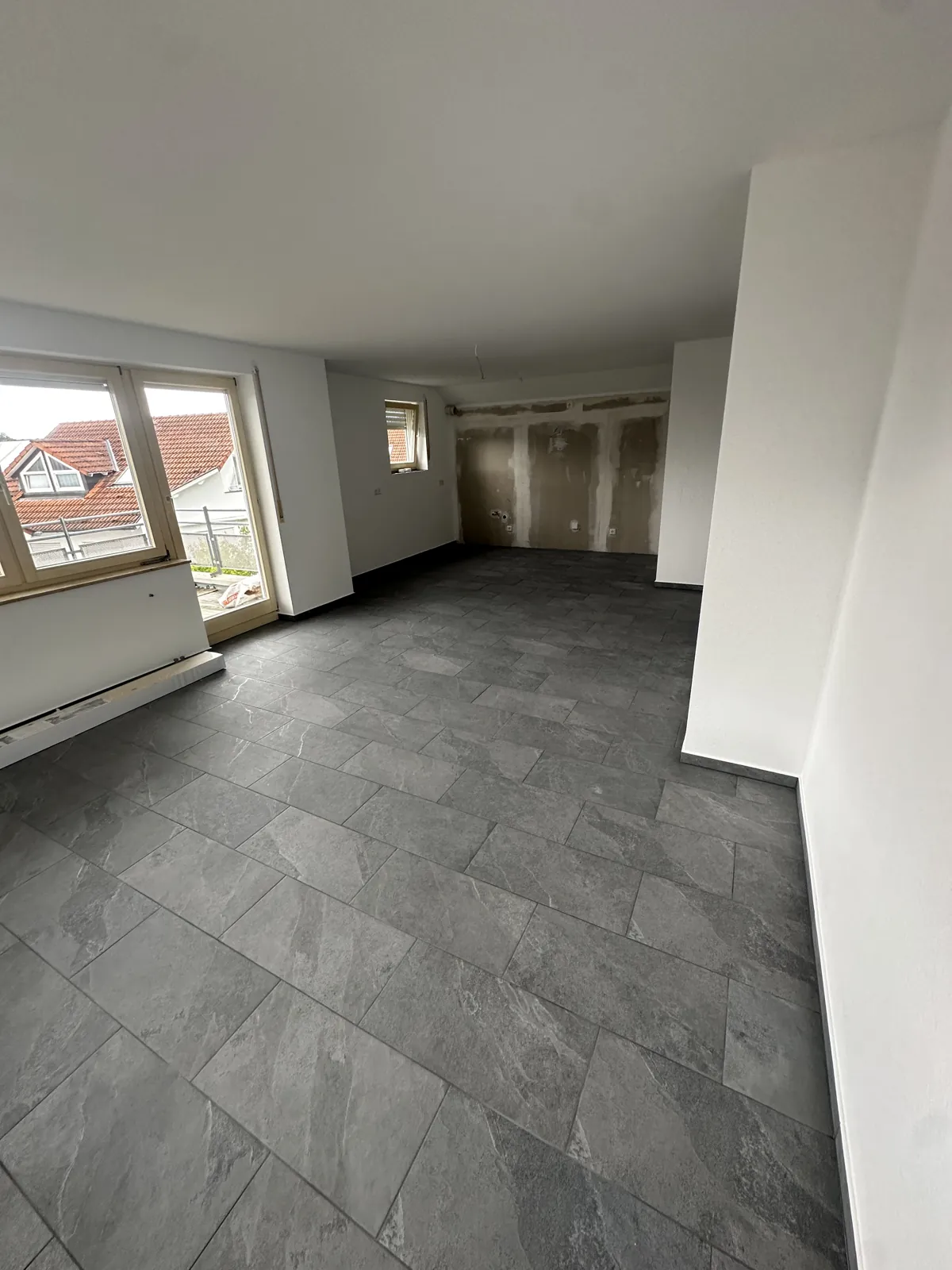 Saniertes Wohnzimmer mit Balkontür und grauen Feinsteinzeug-Fliesen im Format 30x60