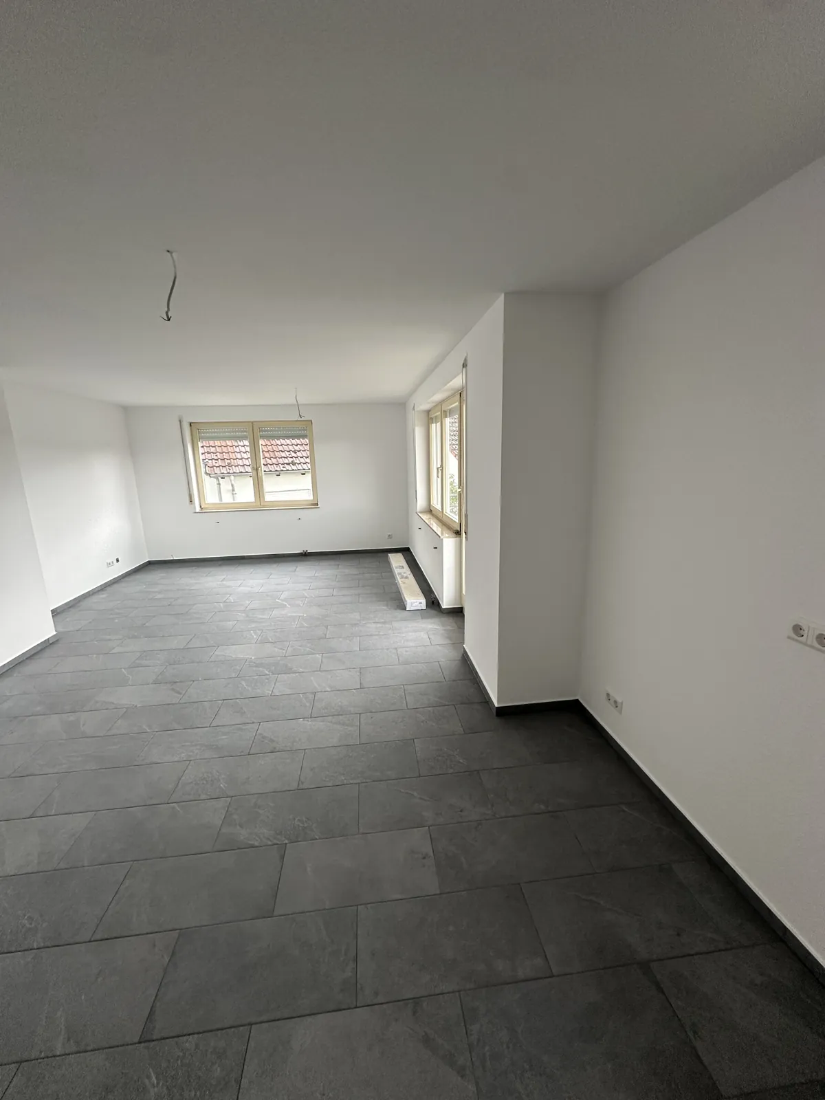 Fertiges Wohnzimmer mit weißen Wänden, neuen Fenstern und grauem Fliesenboden