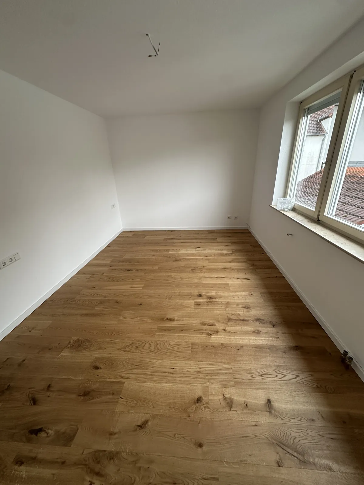 Renoviertes Zimmer mit neuem Holzboden, weißen Wänden und Holzfenster