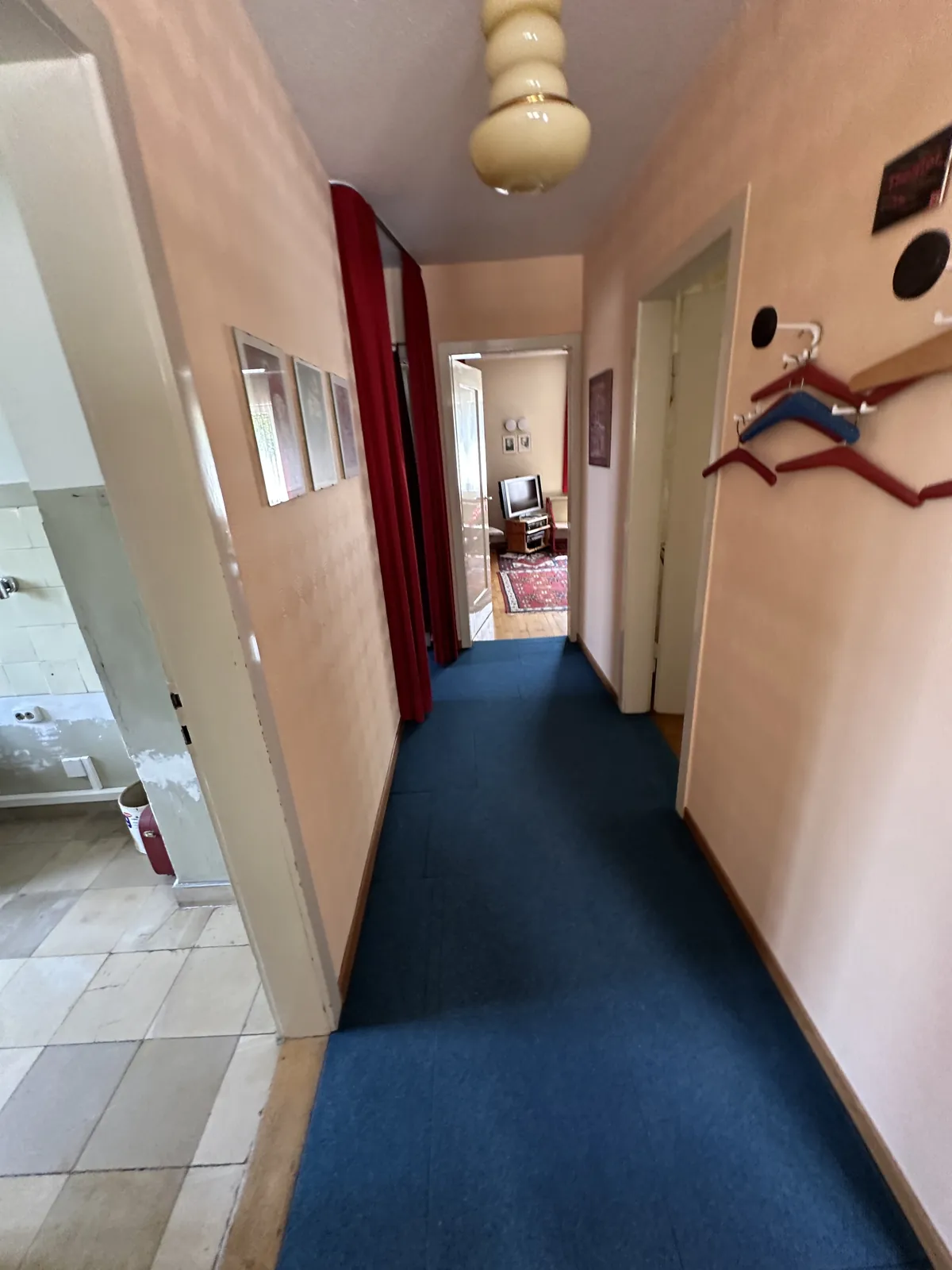 Alter Flur mit blauem Teppichboden und Garderobe vor der Kernsanierung