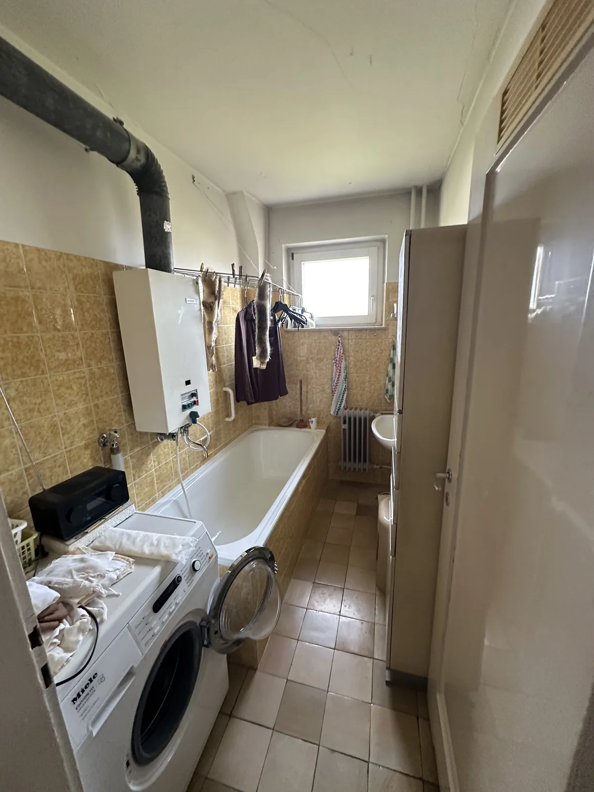 Altes Badezimmer mit Gastherme, Badewanne und Waschmaschine vor der Sanierung