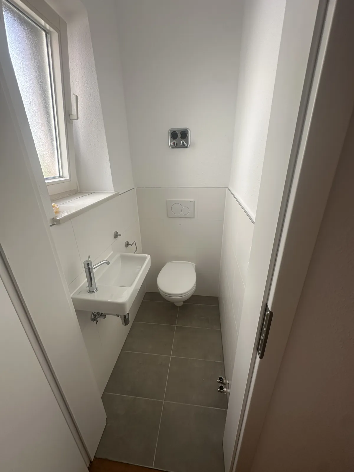 Neues Gäste-WC mit Wand-WC, Handwaschbecken und grauem Fliesenboden